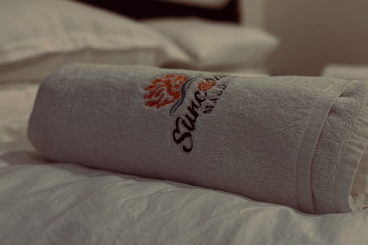 A neatly folded towel with a logo on a bed.