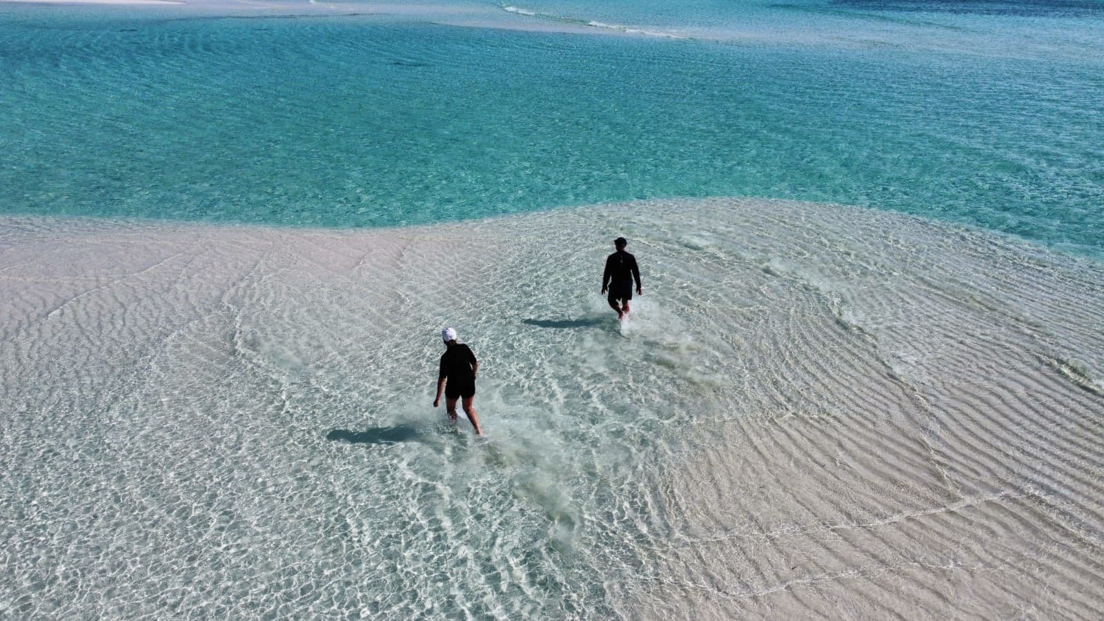 Une plage où deux personnes se promènent sur le sable.