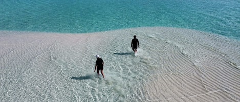 A beach with two people walking on the sand.