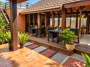 An outdoor patio with wooden tables and chairs, surrounded by potted plants and a tiled floor. - Suncoral Maldives (Kondey)
