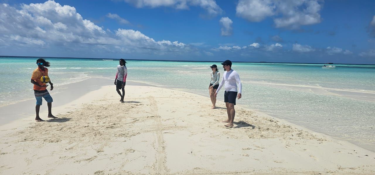 A beach with people, clear turquoise water, and a boat in the distance.
