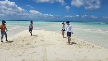 A beach with people, clear turquoise water, and a boat in the distance.