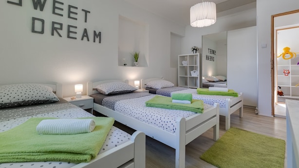 A modern bedroom with three beds, each with a different patterned bedspread. There is a wall-mounted shelf with decorative items and a mirror. - Holiday Home Green Gold (Brinje)
