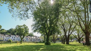 Un parco con alberi grandi, una zona erbosa e una fila di case bianche sullo sfondo.