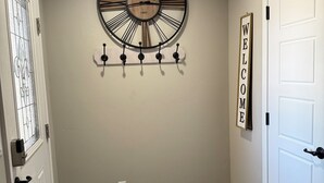 A hallway with a wooden floor, a wall-mounted clock, a coat rack, and a 'WELCOME' sign. - Beautiful and cozy home, perfect for long stay (Alamogordo)