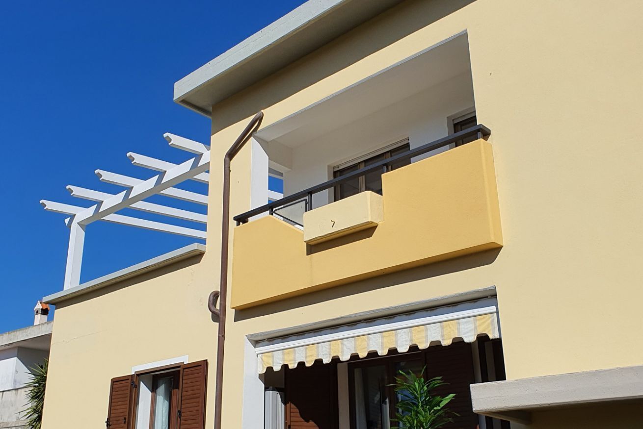 Ein gelbes Gebäude mit Balkon, Fensterläden und einer weißen Markise.