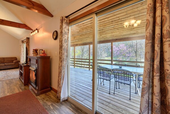 A cozy living room with a fireplace, a sofa, and a view of an outdoor deck with a table and chairs.