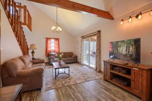 A cozy living room with a wooden staircase, a sofa, a coffee table, and a TV on a wooden stand.