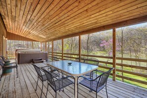 A covered outdoor deck with a wooden ceiling, a glass-top table, and metal chairs.