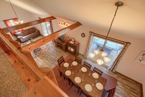 A spacious dining area with a wooden table set for six, a sofa in the background, and a fireplace.
