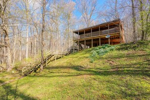 A wooden cabin with a staircase leading up to a deck, surrounded by trees.