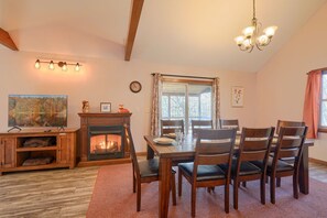 A dining area with a wooden table, four chairs, a fireplace, and a chandelier.