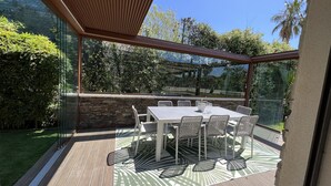 A glass-enclosed patio with a stone wall, a white table, and wicker chairs. - Capleouna- La Cabane, 3 bedrooms, Cap d'Antibes. (Antibes)