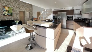 A modern kitchen with a central island, built-in appliances, and a stone accent wall. - Capleouna- La Cabane, 3 bedrooms, Cap d'Antibes. (Antibes)