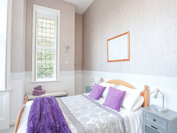 A bedroom with a bed, a nightstand, a window, and a wall-mounted mirror.