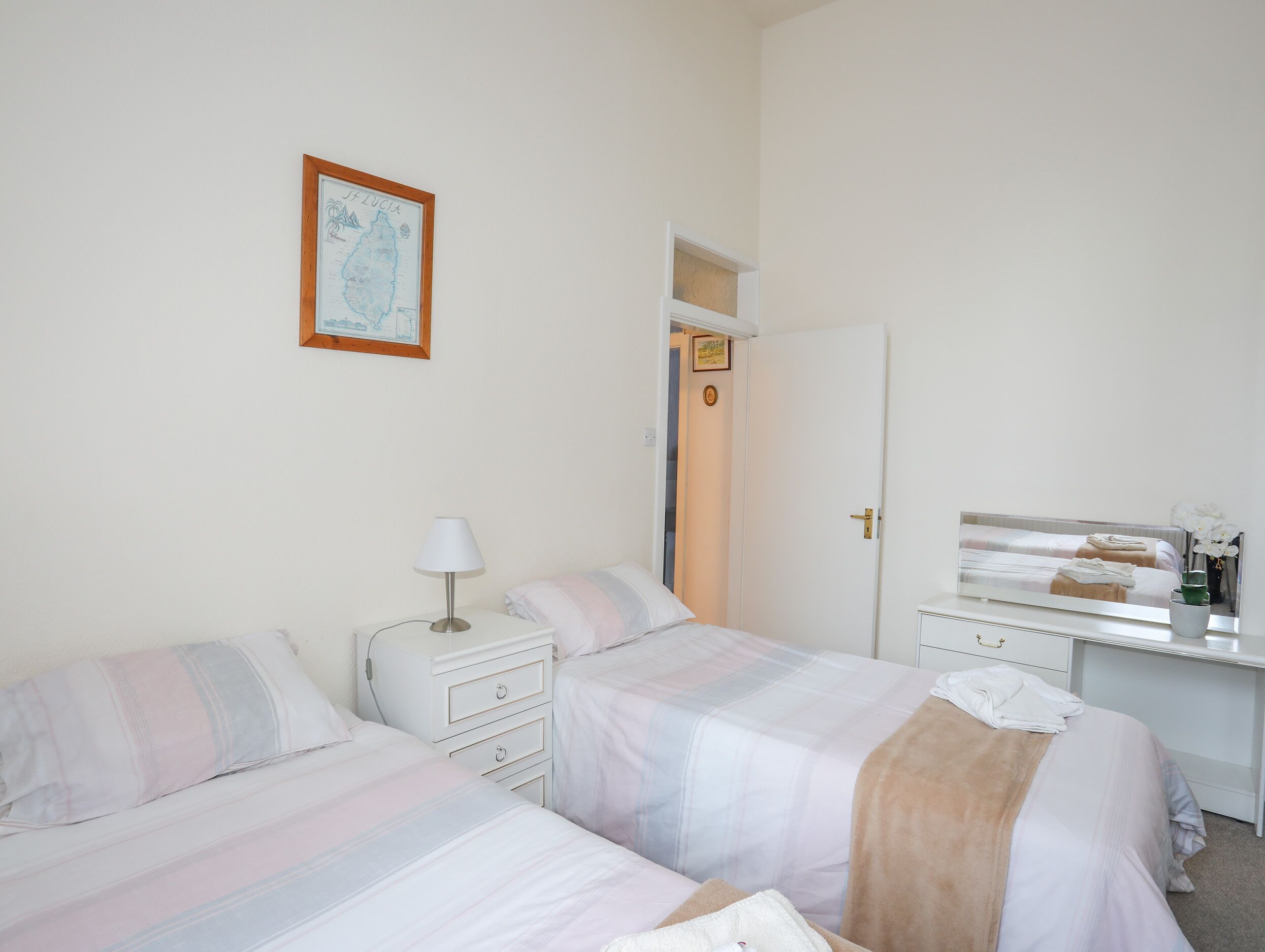 Une chambre avec deux lits, une table de chevet avec une lampe, une commode et un grand miroir.