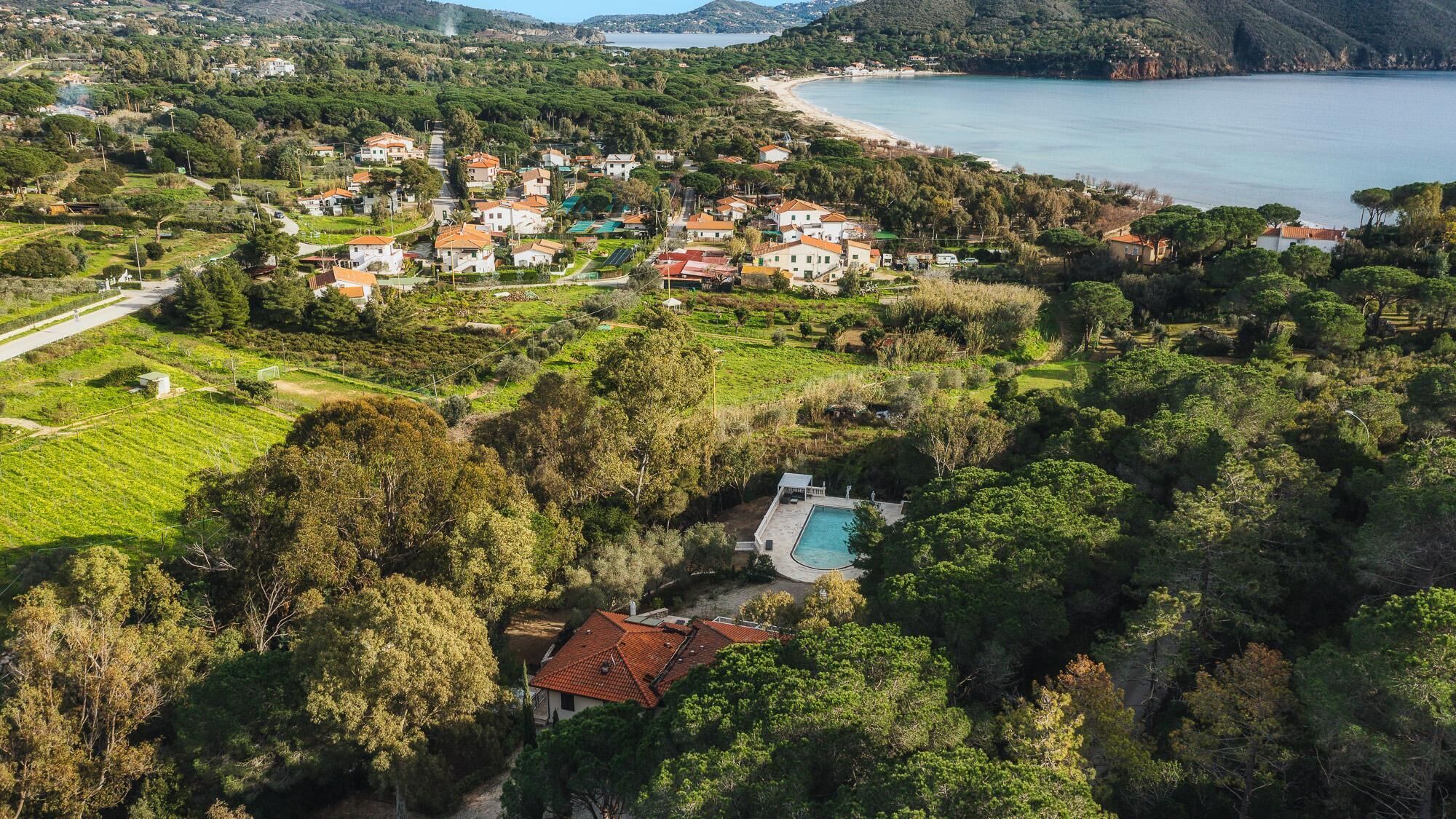 Vista aérea de uma área residencial costeira com casas, piscina e praia.