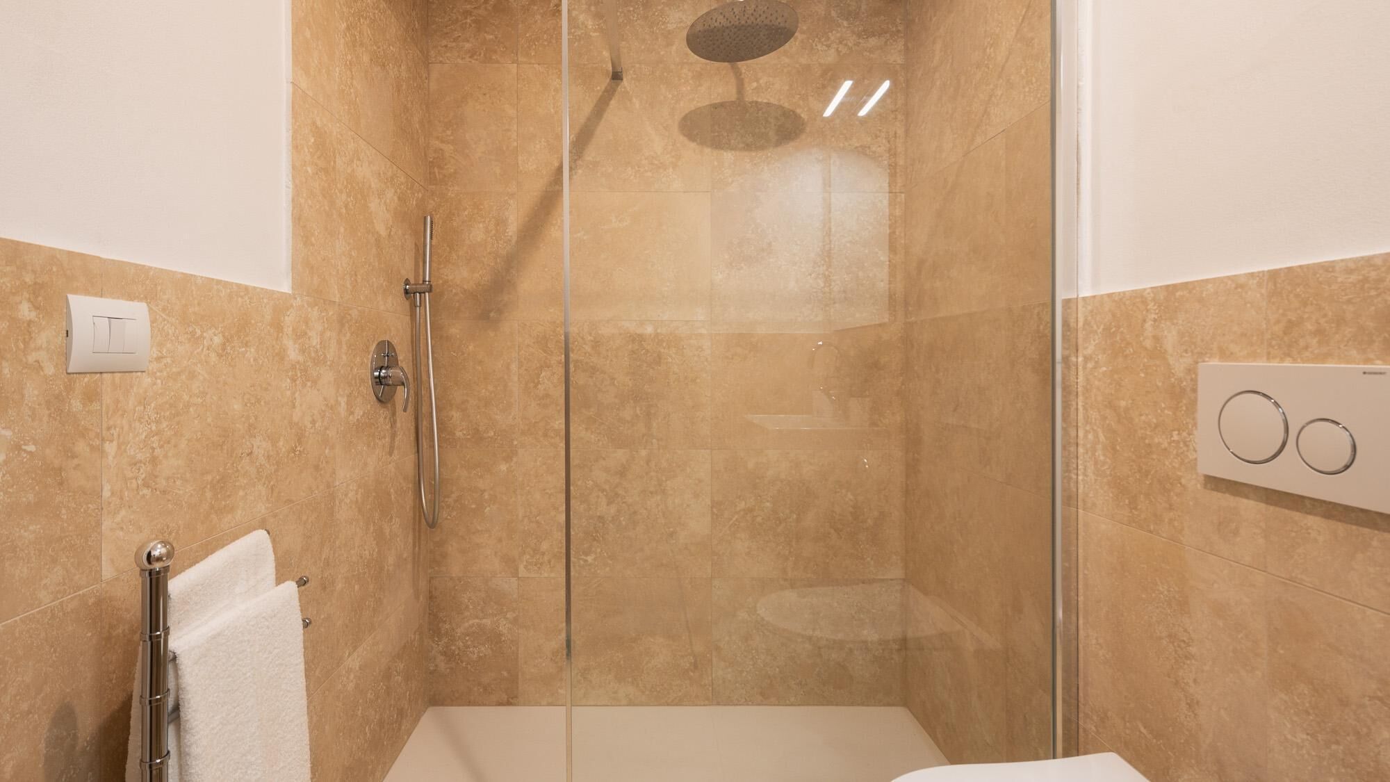 Un baño moderno con cabina de ducha de vidrio, un perchero y un panel de control.
