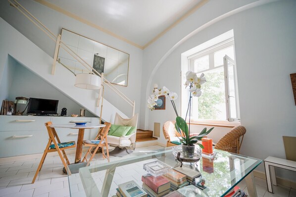 Relax in this spacious room with a high ceiling, featuring a comfortable chair by the window and a cozy reading nook.