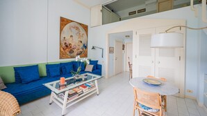 Un soggiorno con un divano blu, un tavolino in vetro con libri, un quadro appeso alla parete e un'area pranzo con tavolo e sedie.