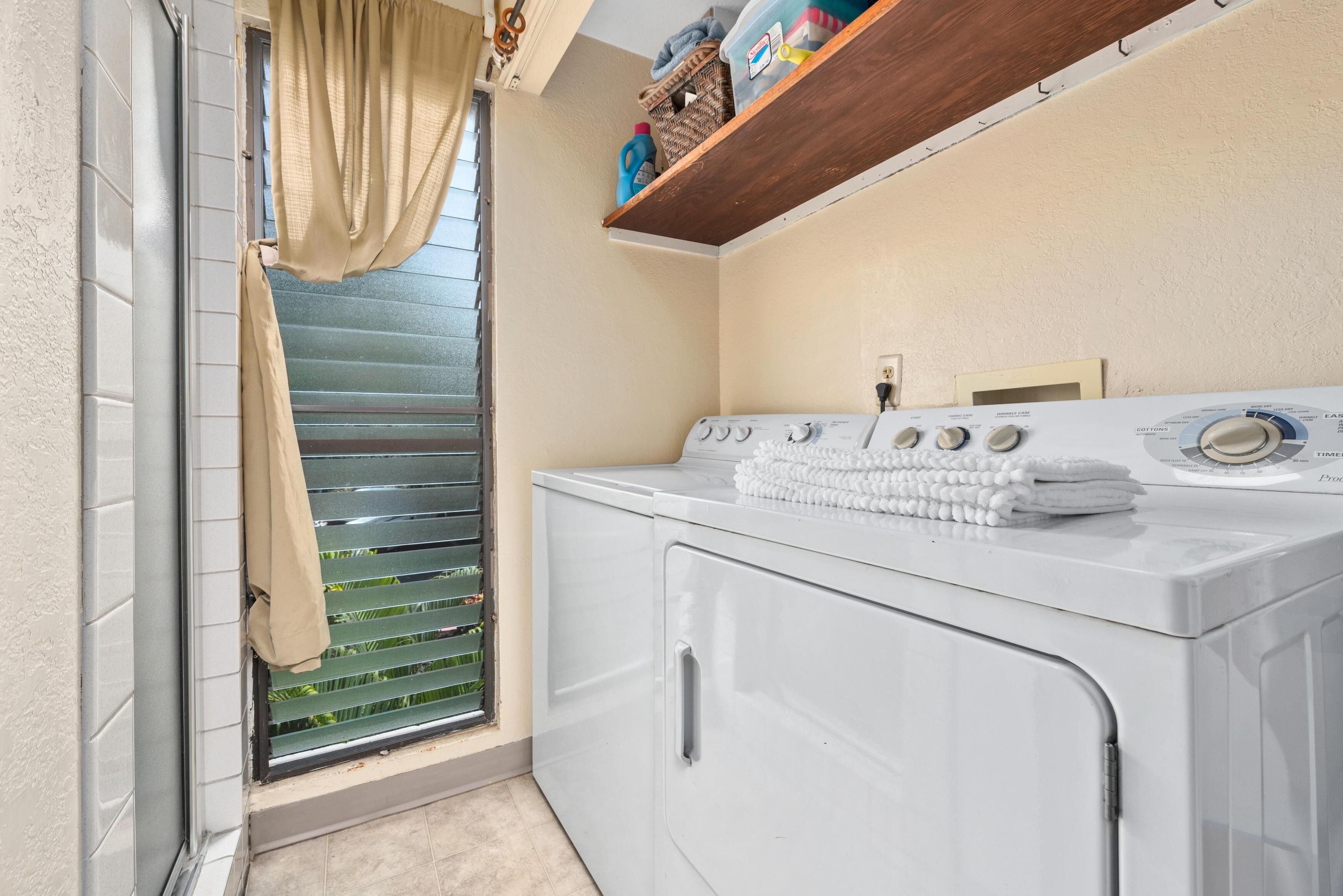 A laundry room with a washing machine, a drying rack, and a window with blinds.