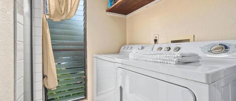 A laundry room with a washing machine, a drying rack, and a window with blinds.