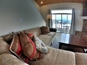 Relax in this inviting living room with a sofa, coffee table, and fireplace, offering a serene view of the surrounding landscape.