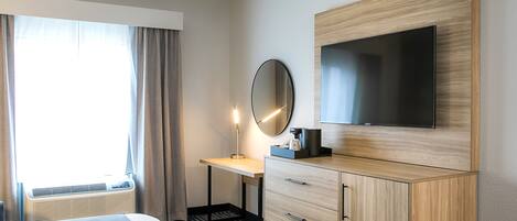 A hotel room with a bed, a desk with a chair, a TV, a mirror, and a wardrobe.