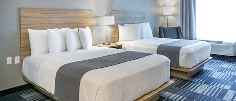 A hotel room with two beds, a nightstand with a lamp, a window with curtains, and a patterned carpet.