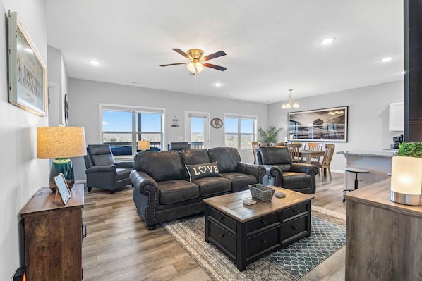 A spacious living room with a dark leather sofa, a coffee table, and a ceiling fan.