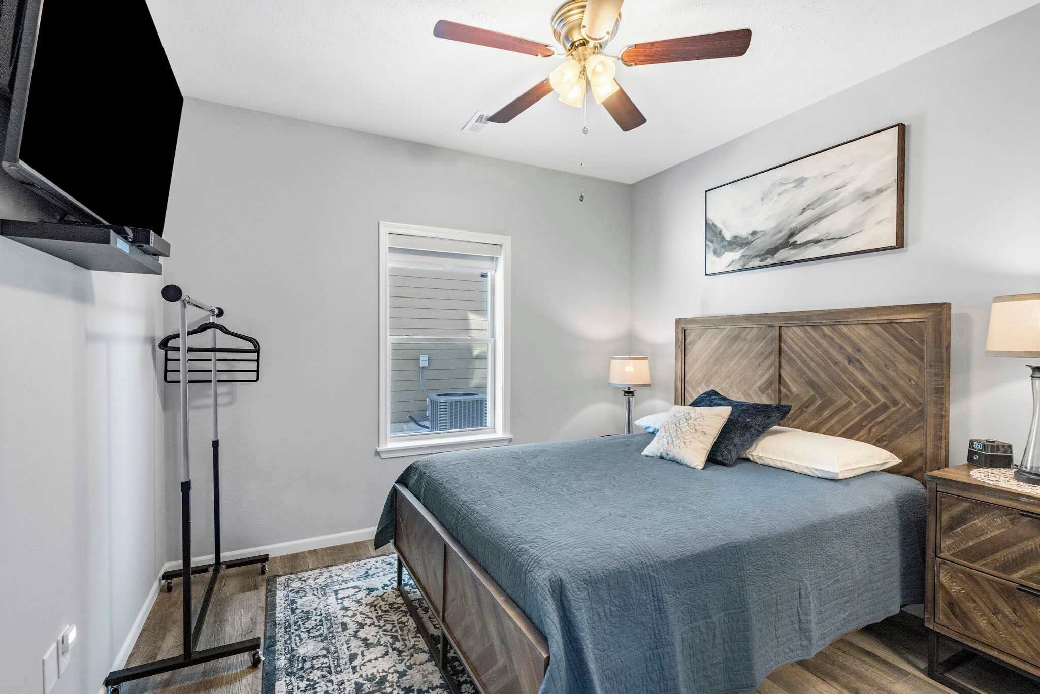 Une chambre à coucher avec un lit, un ventilateur de plafond, une fenêtre, une table de chevet, une lampe et un tableau au mur.