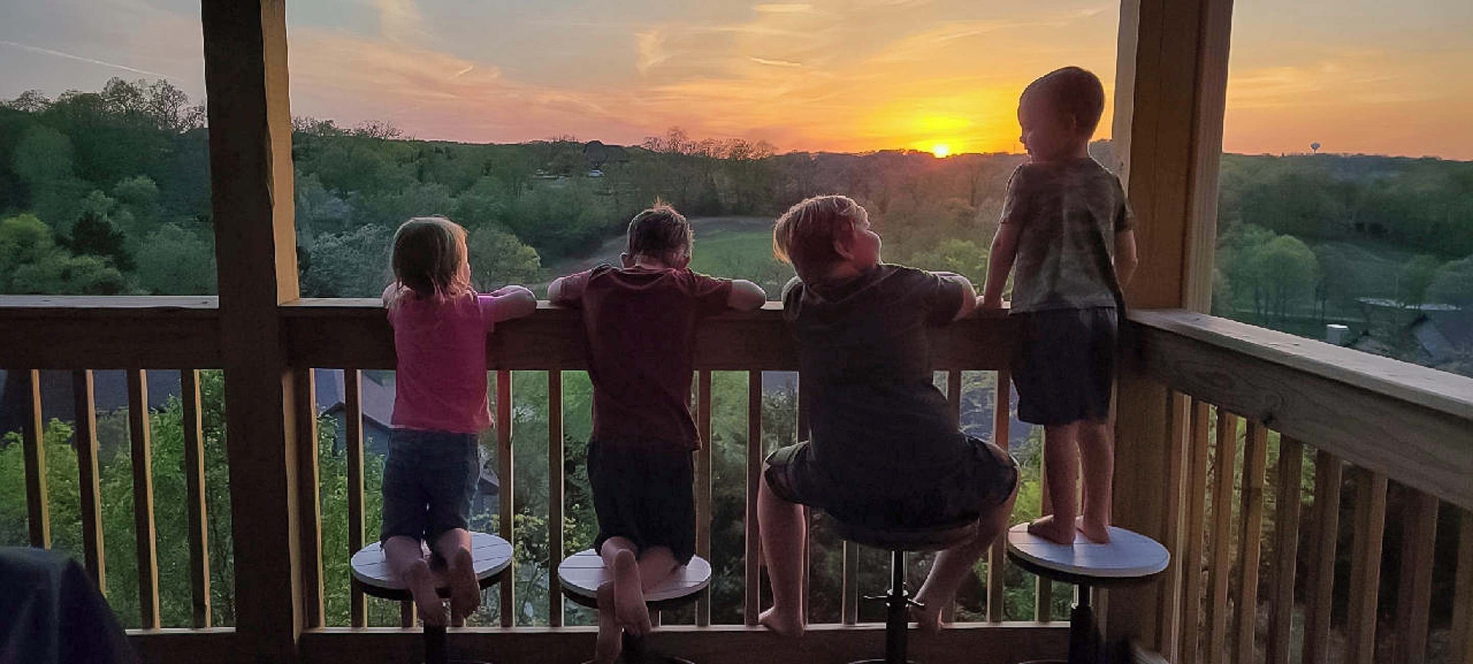 A balcony with four children looking out at a sunset.