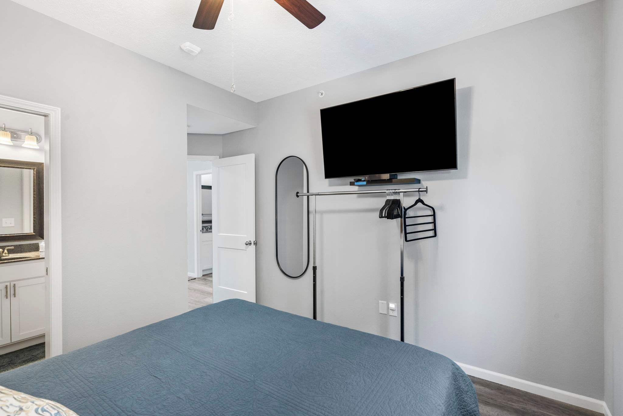 Ein Schlafzimmer mit einem Bett, einem an der Wand montierten Fernseher und einer Tür zu einem anderen Raum.