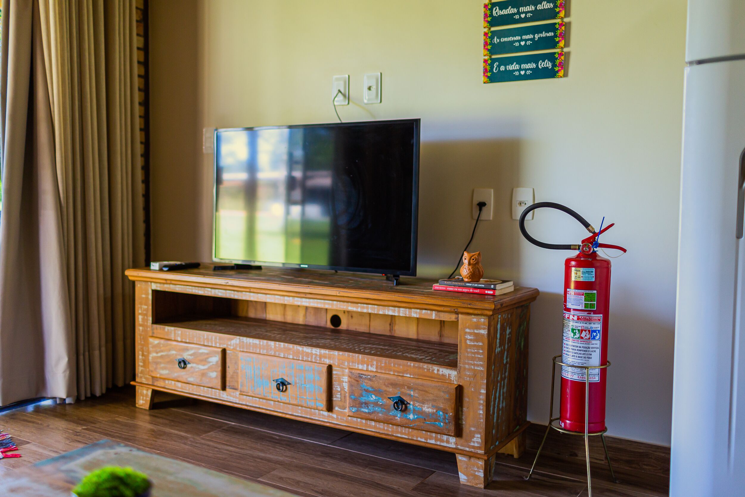 A wooden entertainment center with a flat-screen TV, a fire extinguisher, and a small statue.