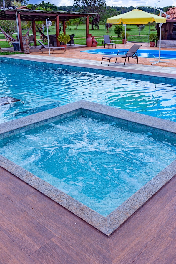 Una piscina con hidromasaje, sillas de descanso y una zona de estar cubierta.