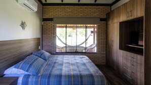A bedroom with a bed, a TV cabinet, and a hammock by a brick wall window. - Villaggio dos Pássaros (Paranoa)
