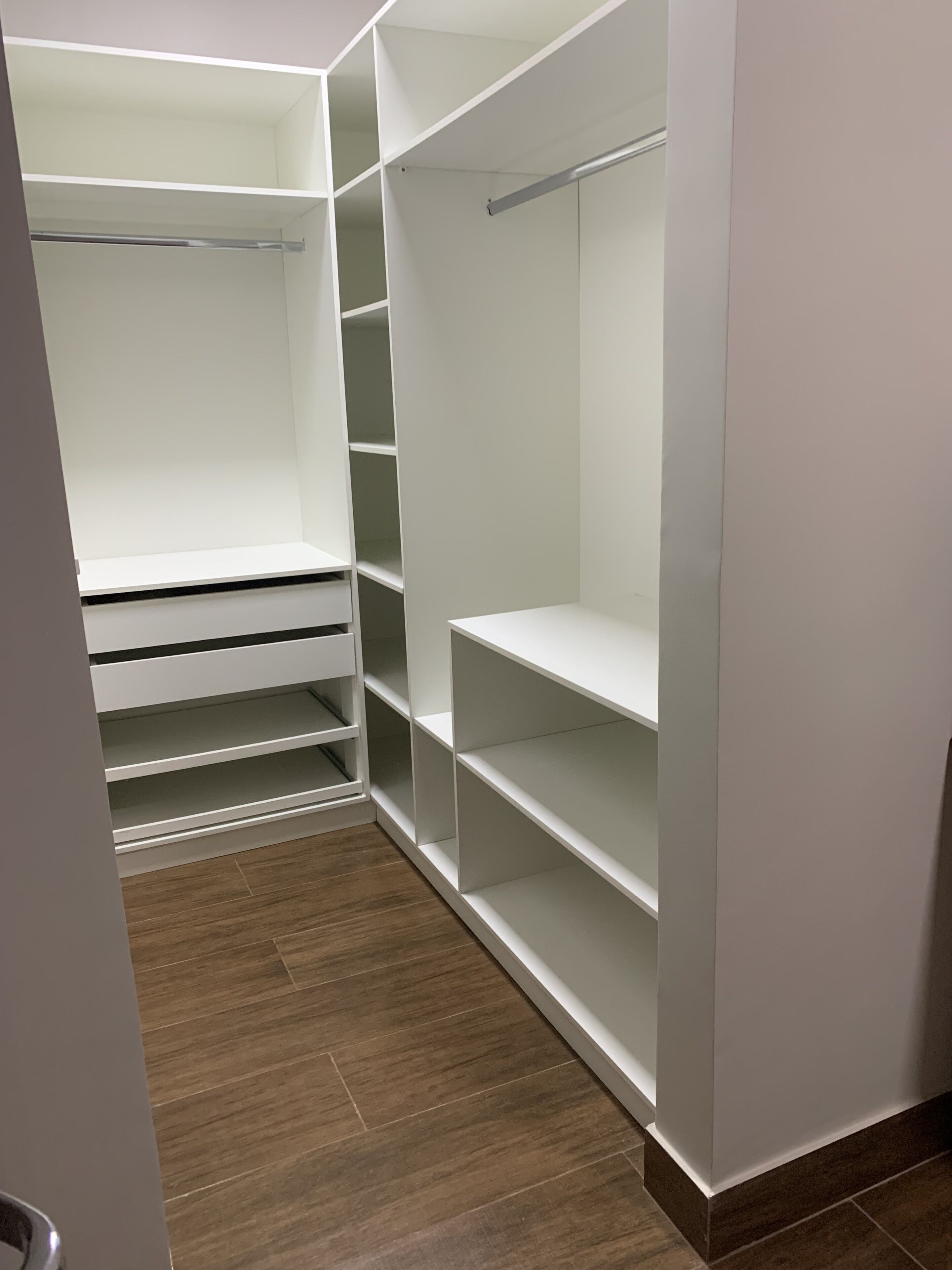 Ein begehbarer Kleiderschrank mit mehreren Regalen und Platz zum Aufhängen, Holzboden und eine weiße Tür.