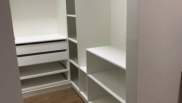 Ein begehbarer Kleiderschrank mit mehreren Regalen und Platz zum Aufhängen, Holzboden und eine weiße Tür.