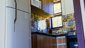 A compact kitchen with wooden cabinets, a white refrigerator, a microwave, and a stove.