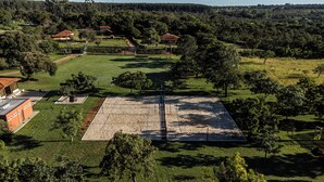 An aerial view of a rural property with a large open field, several buildings with red roofs, and surrounding greenery. - Villaggio dos Pássaros (Paranoa)