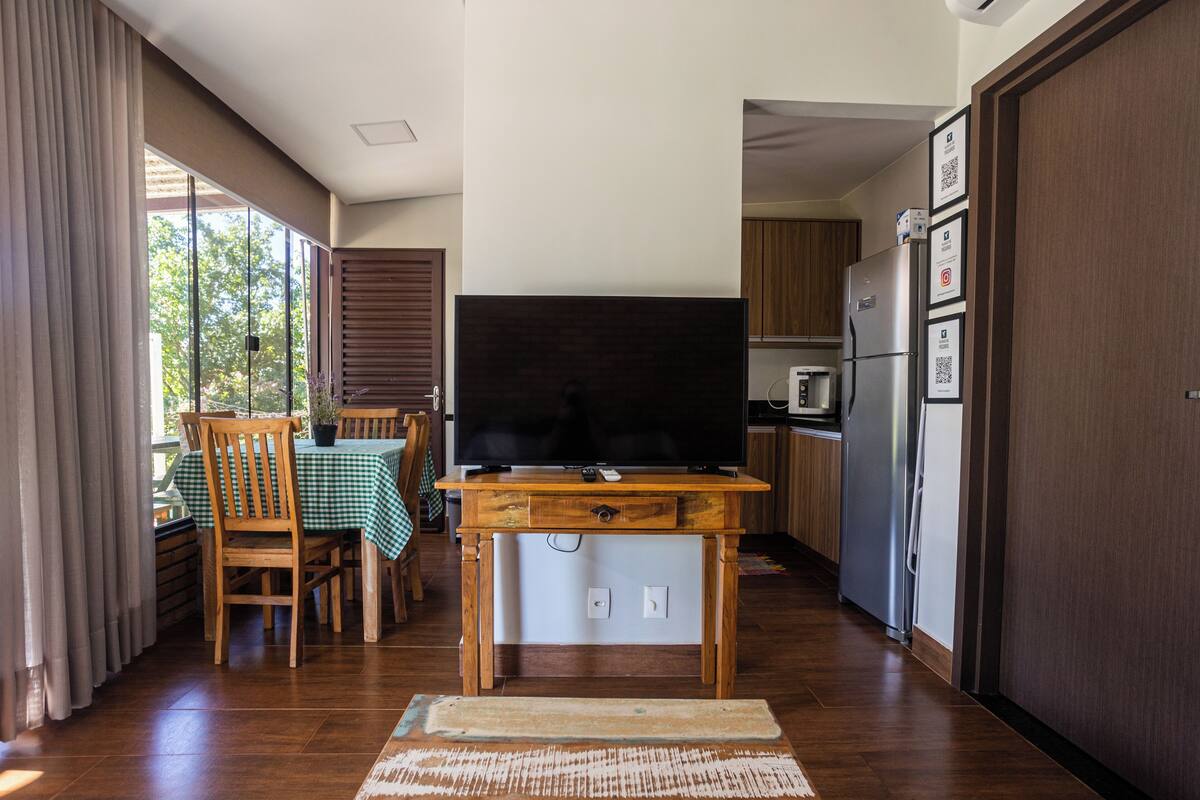 A compact kitchen with a wooden table, a flat-screen TV, and a refrigerator.