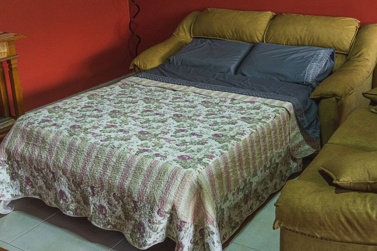 A bed with a floral bedspread, a brown headboard, and a brown armchair.