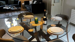Un coin repas avec une table en verre dressée pour quatre personnes, entourée de chaises modernes. Une bouteille de vin et des verres sont posés sur la table.
