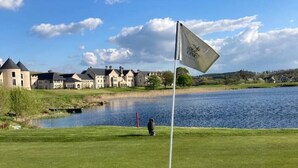 Un terrain de golf avec un drapeau, un étang et des maisons en arrière-plan.