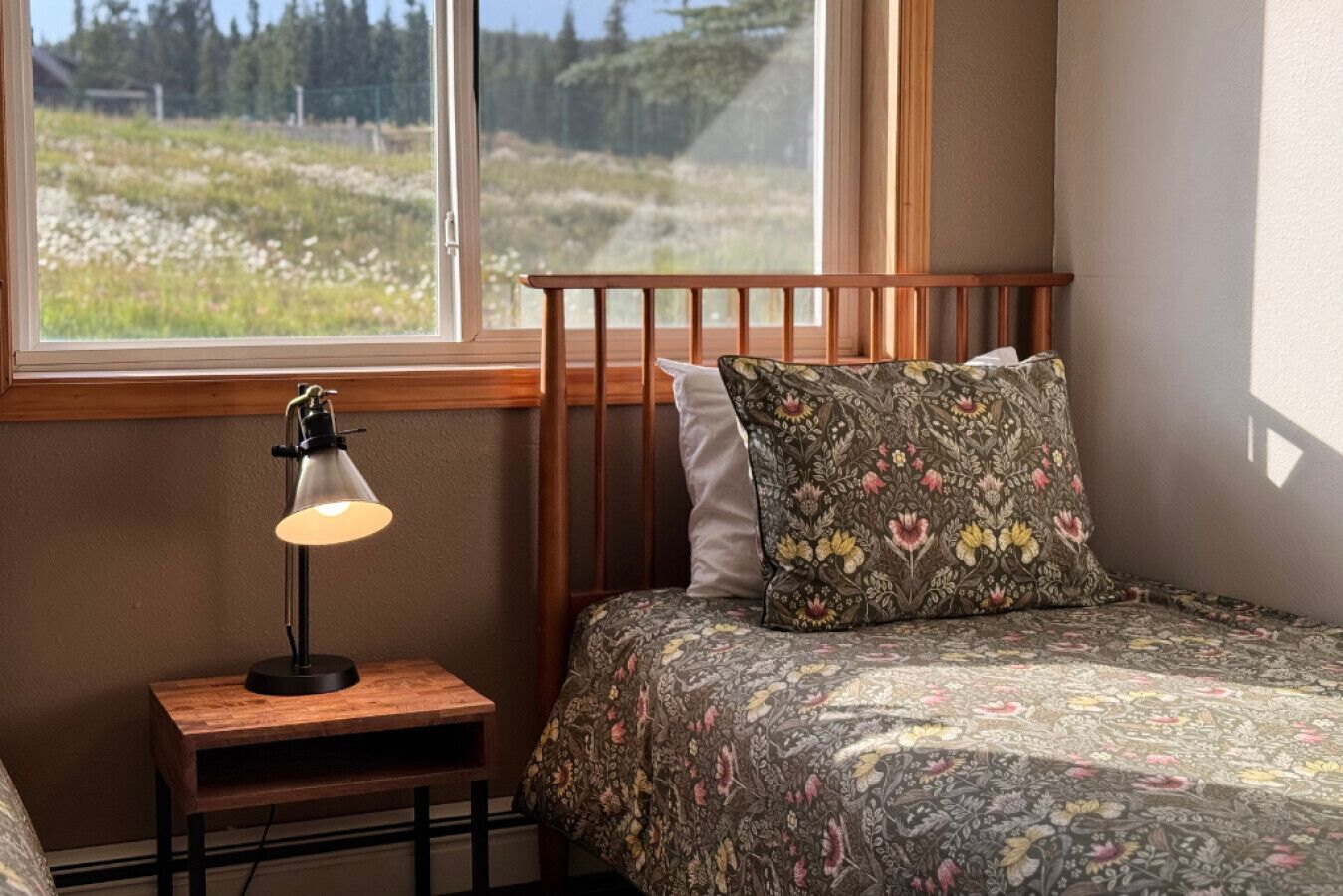 A bedroom with a wooden headboard, a bedside table with a lamp, and a floral-patterned bedspread.