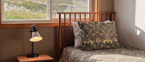A bedroom with a wooden headboard, a bedside table with a lamp, and a floral-patterned bedspread.