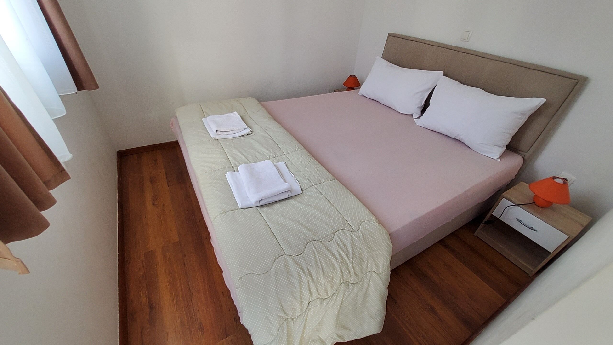 Un dormitorio con cama, mesita de noche, lámpara y ventana con cortinas.