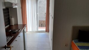 Una cocina pequeña y luminosa con armarios blancos, una encimera de madera y vistas a un balcón con pared de ladrillo.