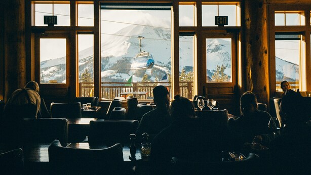 Un restaurante con amplios ventanales que dan a una montaña nevada y un telesilla.