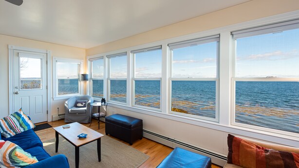 Ein Zimmer mit großem Fenster mit Meerblick, einem blauen Sofa, einem kleinen Tisch und einem Stuhl.